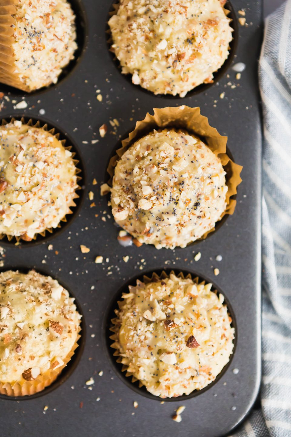 An overhead shot of six gluten-free almond poppyseed muffins in a dark muffin tin. 
