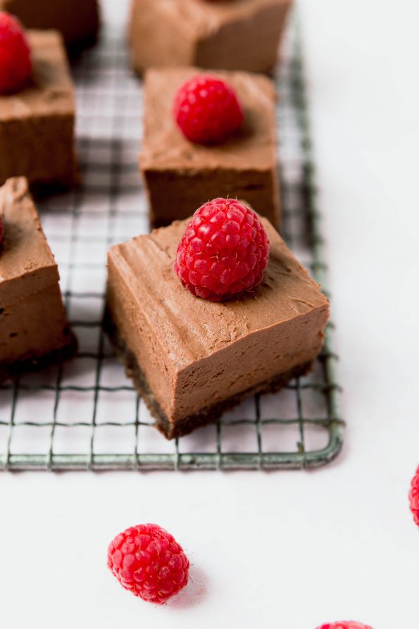 Chocolate cheesecake bars layered on a grated serving dish. Raspberries are placed on top.