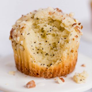 Up close shot of a gluten-free almond poppyseed muffin on a small cupcake pedestal. There is a big bite taken out of the front of the muffin.