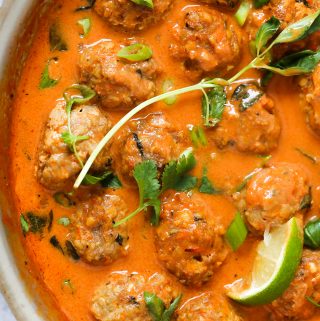 An overhead shot of a turkey meatballs in a thai coconut curry sauce. There is thai basil, green onions, and lime wedges scattered throughout.