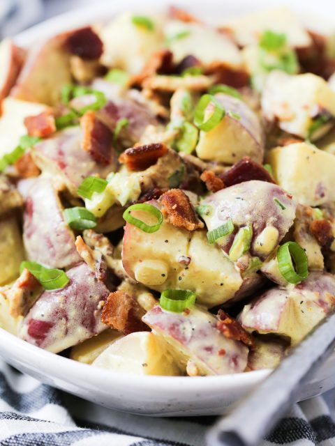 Up close shot of honey mustard potato salad garnished with bacon and green onions.