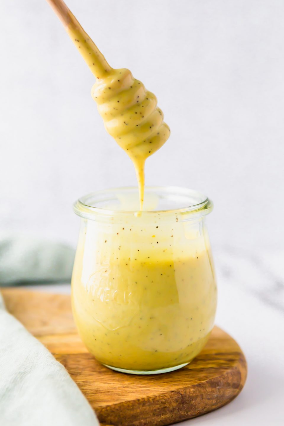 Honey mustard dressing in a small jar with a honey dipper. The dressing is dripping onto the jar. 