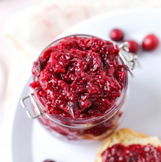 Overhead photo of cranberry jam made with chia seeds. There are whole cranberries and toast with the jam on it in the background.