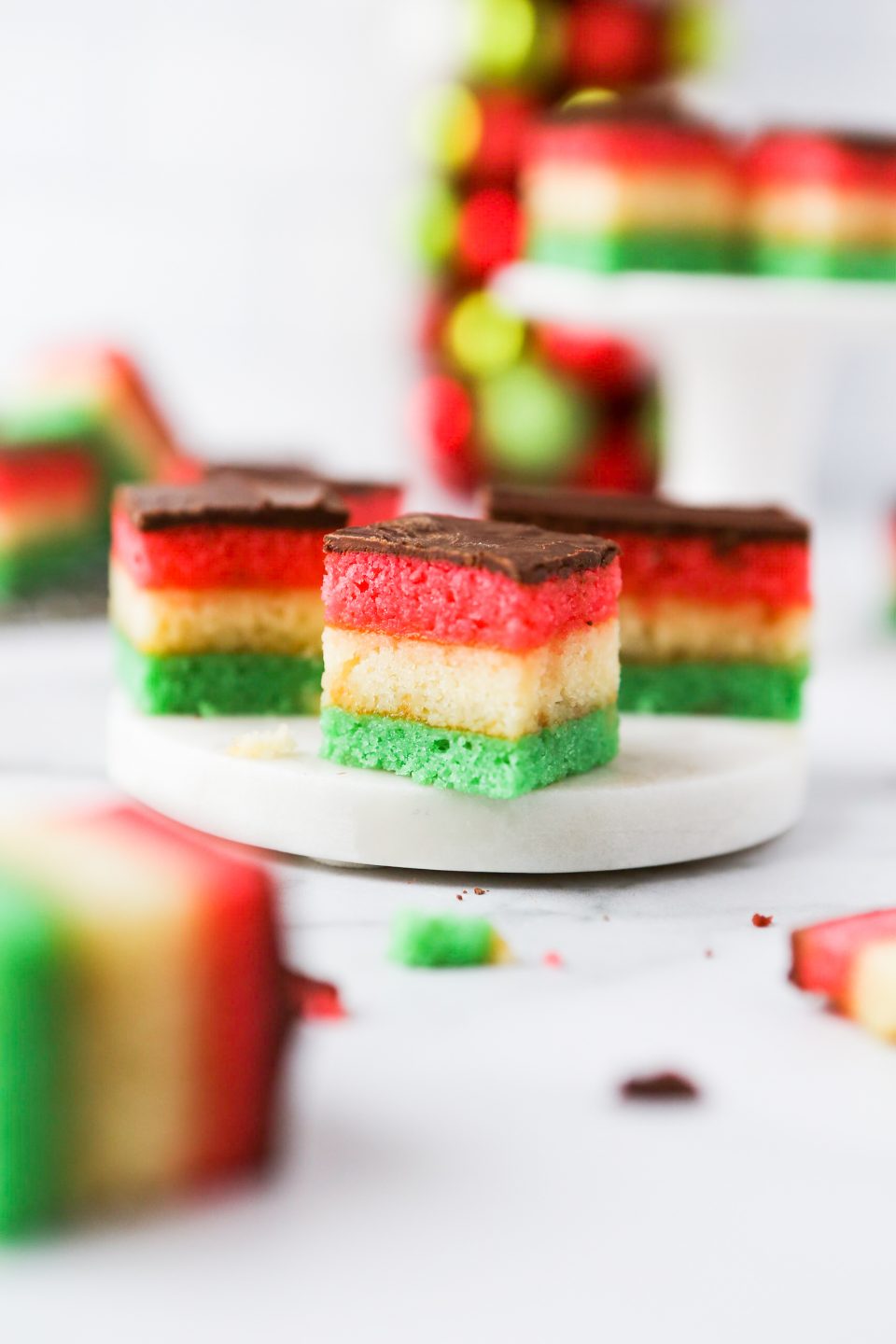 A photo showing gluten-free Venetian cookies which is 3 layers of almond cake with apricot jam between each layer and then coated in semi-sweet chocolate. They are cut into small pieces so you can see the layered colors of red, white, and green. 