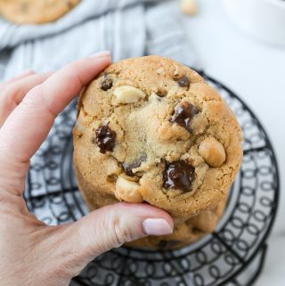 A hand holding on to a freshly baked macadamia nut chocolate chunk cookies.