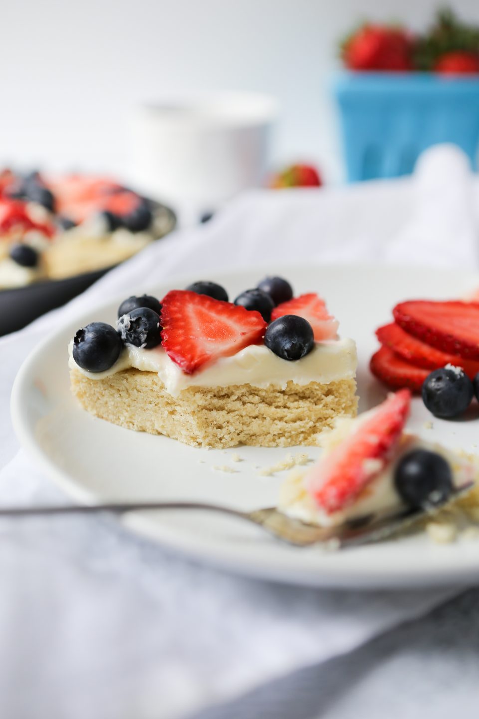A photo of a slice of gluten-free fruit pizza with a sugar cookie crust, a layer of cream cheese frosting, and fresh fruit. 